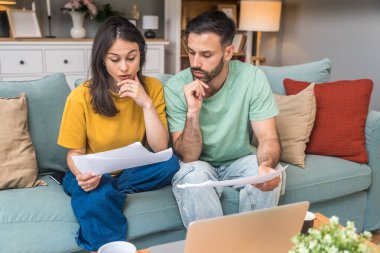 Evde Muhasebe: Dizüstü bilgisayar kullanan mutlu çift, Apartmanda masa başında oturuyor. Genç Aile Vergi Formları, İpotek Belgeleri, Faturalar, Çekler, Dengeler, Faturalar Düzenli