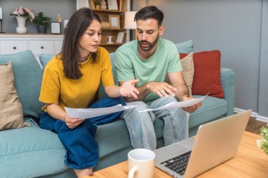 Evde Muhasebe: Dizüstü bilgisayar kullanan mutlu çift, Apartmanda masa başında oturuyor. Genç Aile Vergi Formları, İpotek Belgeleri, Faturalar, Çekler, Dengeler, Faturalar Düzenli