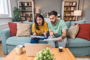 Evde Muhasebe: Dizüstü bilgisayar kullanan mutlu çift, Apartmanda masa başında oturuyor. Genç Aile Vergi Formları, İpotek Belgeleri, Faturalar, Çekler, Dengeler, Faturalar Düzenli