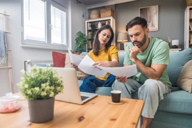 Evde Muhasebe: Dizüstü bilgisayar kullanan mutlu çift, Apartmanda masa başında oturuyor. Genç Aile Vergi Formları, İpotek Belgeleri, Faturalar, Çekler, Dengeler, Faturalar Düzenli