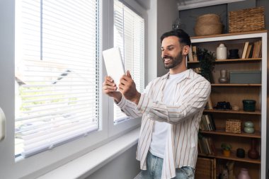 Ofisteki pencerenin yanında dijital tabletle duran genç mutlu adam psikoterapisti, hastadan iyi haberlerle dolu bir e-posta aldıktan sonra heyecanlanıyor. Pozitif çevrimiçi psikoterapi sonuç kavramı