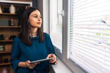 Ofisteki pencerenin yanında dijital tabletle duran mutlu genç kadın psikoterapist hastadan iyi haberlerle dolu bir e-posta aldıktan sonra heyecanlanıyor. Pozitif çevrimiçi psikoterapi sonuç kavramı
