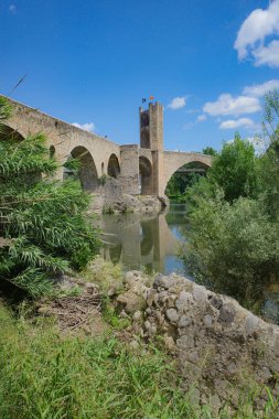 Girona, Spain - 7 July, 2024: Reflections of the medieval Pont Vell bridge on the River Fluvia at Besalu, Catalonia clipart