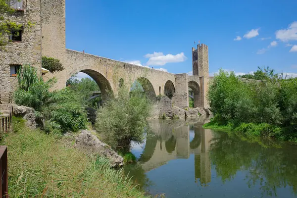 stock image Girona, Spain - 7 July, 2024: Reflections of the medieval Pont Vell bridge on the River Fluvia at Besalu, Catalonia