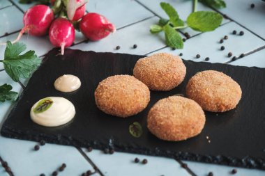 Siyah tahtaya ve mavi fayanslı masaya yerleştirilmiş lezzetli kızarmış sebze köftelerini yakın plan, taze malzemeler ve sebzeler.