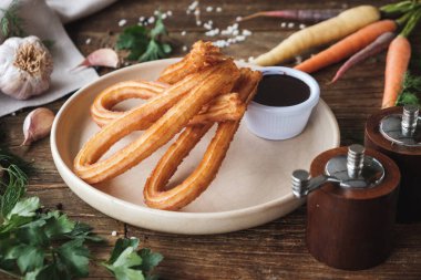 Taze pişmiş, çikolata soslu tatlı churro. Kırsal ahşap bir masa üzerinde, tabağı çevreleyen malzemeler.