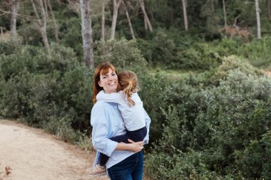 Doğada yürüyen mutlu sevgi dolu bir aile. Anne ve kızı çocuk sarılıp vakit geçiriyorlar..