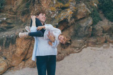 Kumsalda küçük kızıyla oynayan mutlu, genç bir kadın. Anne çocuğuyla vakit geçirir ve birlikte eğlenir. Genç bir ailenin doğal yaz resmi..