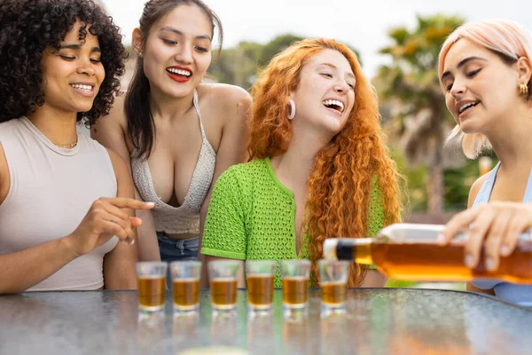 4人の幸せな女の子は テーブルに座って 1つの注ぎラム酒 ラムやロン とショットグラスに 一緒に祝う若い女性の混合レースグループ パーティー 夏休みの概念 — ストック写真