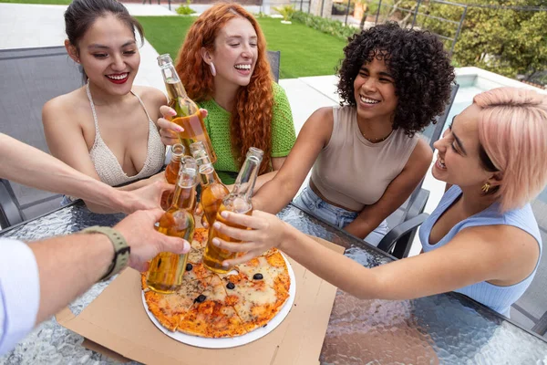 A multiethnic group of happy people joyfully clink light beers, enjoying a good company during summer vacation. Dinner with pizza outdoors. The atmosphere of festivity and celebration. POV image.
