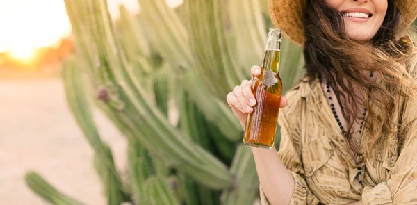 サボテンに囲まれたメキシコの砂漠でビールを楽しむ気の利いた女の子 ビールを持っている若い女性の笑顔 コピースペースとイメージ — ストック写真