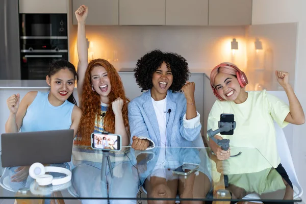 Four beautiful women, diverse bloggers collaborate on online project, showing immense joy, celebration success, good cooperation result, partnership teamwork and victory gesture.