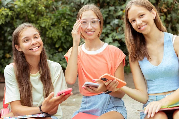 三位14岁至15岁的少女坐在户外 专心致志地听着手机 树立了现代青少年 生活方式 教育以及小玩艺儿和社交媒体的影响的典范 — 图库照片