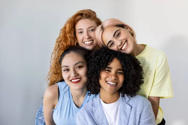A group of beautiful young women from different races, smiling and looking at the camera against a white wall backdrop. Concept of cross-cultural friendship and diverse beauty. Focus on African girl.