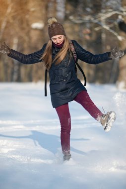 Karlı bir kış parkında gülümseyen ve kar kusan genç bir kadın. Güneşli bir hava. Kış mevsimi.