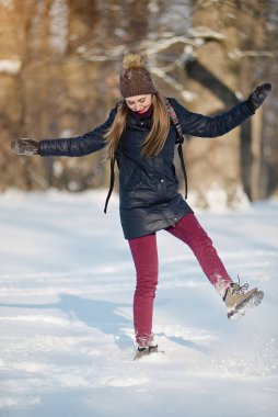 Karlı bir kış parkında gülümseyen ve kar kusan genç bir kadın. Güneşli bir hava. Kış mevsimi.