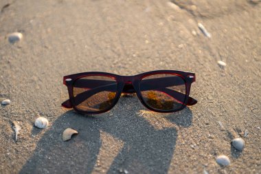 Güneş gözlüğü gün batımında kumsalda yatar.