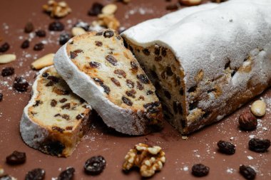 Dilimlenmiş Stollen. Geleneksel kek tozlu pudra şekerli kurutulmuş meyve ve fındıklı kahverengi arka planda.