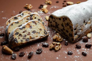 Dilimlenmiş Stollen. Geleneksel kek tozlu pudra şekerli kurutulmuş meyve ve fındıklı kahverengi arka planda.