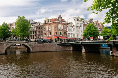 Geleneksel tuğla köprü Amsterdam kanalından geçiyor, tarihi gaçalı evleri ve park edilmiş bisikletleri var.