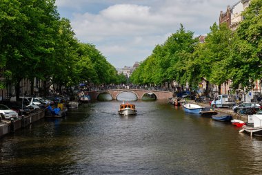 Küçük özel bir tekne Amsterdam kanalında klasik bir tuğla kemer köprüsüne doğru yol alıyor.