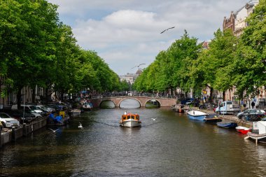 Küçük özel bir tekne Amsterdam kanalında klasik bir tuğla kemer köprüsüne doğru yol alıyor.