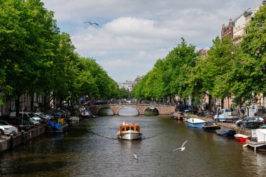 Amsterdam, Hollanda - 21 Mayıs 2025: Küçük özel tekne Amsterdam kanalında klasik tuğla kemer köprüsüne doğru ilerliyor