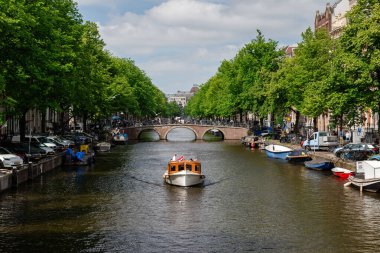 Amsterdam, Hollanda - 21 Mayıs 2025: Küçük özel bir tekne Amsterdam kanalında klasik tuğla kemerli bir köprüye doğru ilerliyor