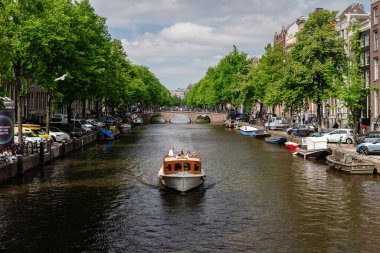 Amsterdam, Hollanda - 21 Mayıs 2025: Küçük özel bir tekne Amsterdam kanalında klasik tuğla kemerli bir köprüye doğru ilerliyor