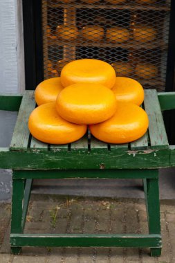 Tahta bir stantta sergilenen sarı-turuncu kabuklu geleneksel Gouda peyniri tekerlekleri.