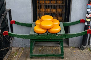 Tahta bir stantta sergilenen sarı-turuncu kabuklu geleneksel Gouda peyniri tekerlekleri.