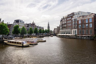 Amsterdam, Hollanda - 21 Mayıs 2025: Ön planda demirlemiş çok sayıda tur teknesinin ve arka planda tarihi Hotel De L 'Europe' un bulunduğu Amsterdam kanalı