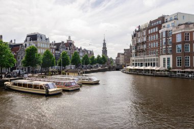 Amsterdam, Hollanda - 21 Mayıs 2025: Ön planda demirlemiş çok sayıda tur teknesinin ve arka planda tarihi Hotel De L 'Europe' un bulunduğu Amsterdam kanalı
