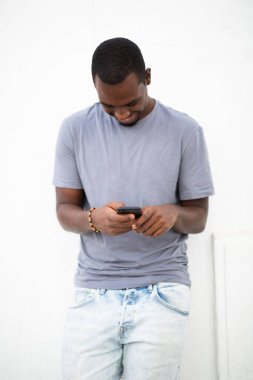 Beyaz arka planda cep telefonu kullanan gülümseyen Afrikalı genç adamın portresi.