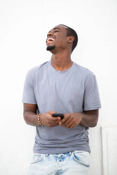 年轻快乐的非洲男子拿着手机 望着别处 在白色背景下大笑的画像 — 图库照片