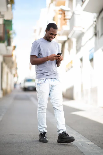 町の外を歩いている間 幸せな若いアフリカ人男性の携帯電話でテキストメッセージの完全な長さの肖像画 — ストック写真