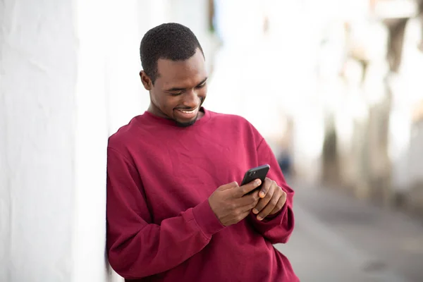 笑顔の若い黒人男性の肖像画壁にもたれ 外の携帯電話でテキストメッセージ — ストック写真