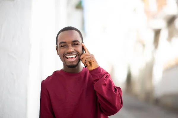 Portret Wesołego Młodego Afrykanina Opierającego Się Ścianę Rozmawiającego Przez Komórkę — Zdjęcie stockowe