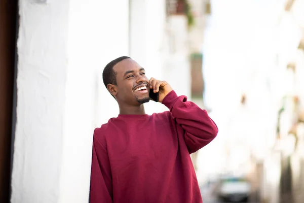 幸せな若いアフリカ系アメリカ人の男性の肖像壁にもたれ 街の屋外でスマートフォンで話す — ストック写真