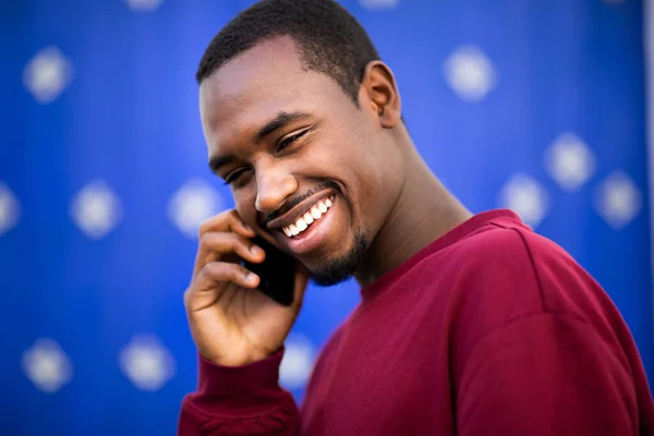 笑着的年轻非洲裔美国人在蓝色背景下用手机交谈的特写 — 图库照片