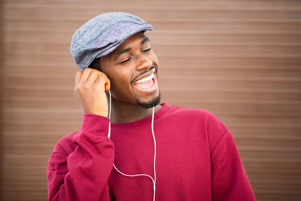 閉じますアップポートレートのハンサムな若いですアフリカ人男性でキャップで音楽を聴くとともにイヤホンに対して茶色の背景 — ストック写真
