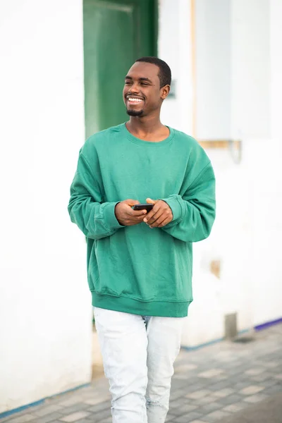 Πορτρέτο Του Χαμογελαστού Νεαρού Αφροαμερικανού Που Κρατάει Κινητό Και Περπατάει — Φωτογραφία Αρχείου