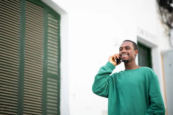 一个快乐的黑人年轻人在外面一边用手机一边笑的形象 — 图库照片