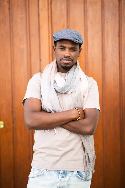 非洲年轻英俊男子的画像 戴着帽子和围巾 双手交叉地站在木制背景下 — 图库照片