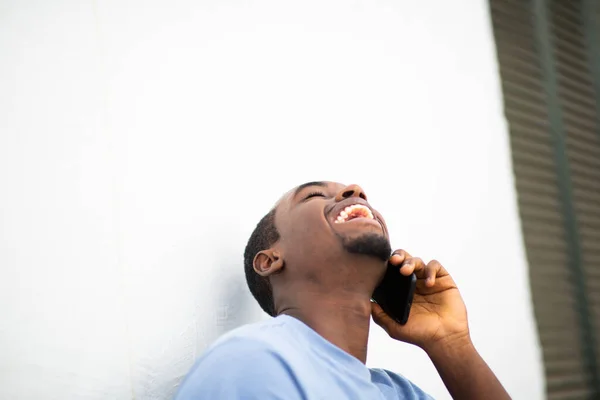 白い壁に対して外の携帯電話で話している若いアフリカ人男性を笑っての肖像画を閉じます — ストック写真