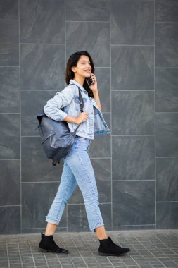 Duvarda yürüyen, cep telefonuyla konuşan mutlu bir kadının tam boy yan portresi. 