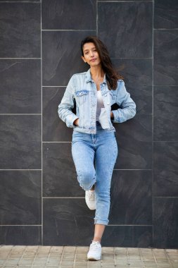 Duvara yaslanmış havalı genç bir kadının tam boy portresi.