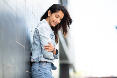 Duvara yaslanmış çekici genç bir kadının yan portresi.