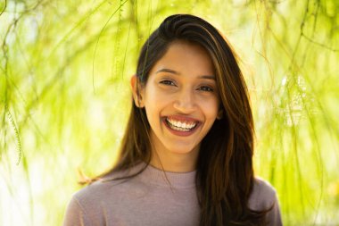 Ağaç kenarında gülümseyen genç bir kadının yüz portresini kapat.