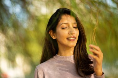 Güzel genç bir kadının ağaç dalına dokunuşunun yakın portresi.